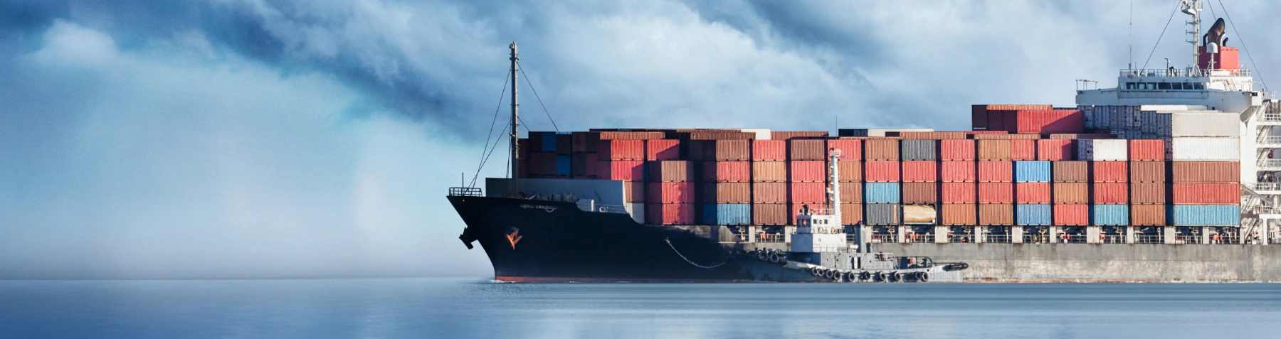 Container Ship Transporting International Ocean Freight Large container ship carrying stacked freight containers across calm ocean waters beside a tugboat.
